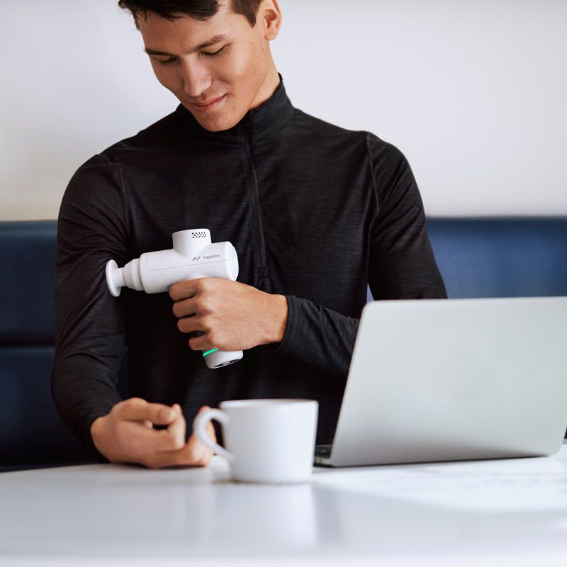 Homme utilisant l'Hypervolt Go 2 en télétravail Homme utilisant l'Hypervolt Go 2 en télétravail